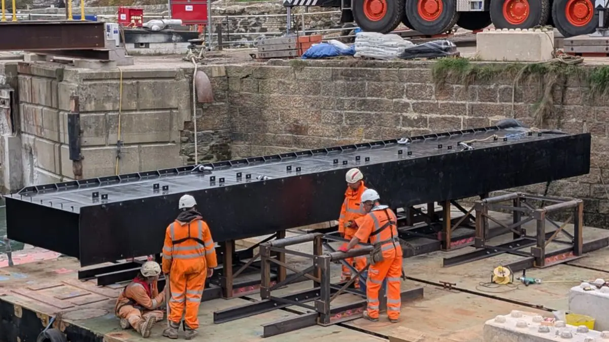 A large section of steel lock gate rests on a floating pontoon with people working in hi vis and hard hats.