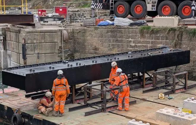 A large section of steel lock gate rests on a floating pontoon with people working in hi vis and hard hats.