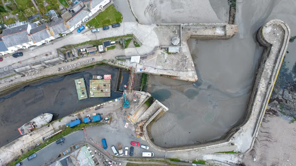 A drone photo showing Charlestown Harbour viewed from directly above while the tide is out. There are two green floating pontoons sitting on the mud of the inner harbour ready to receive the delivery of the new lock gate.