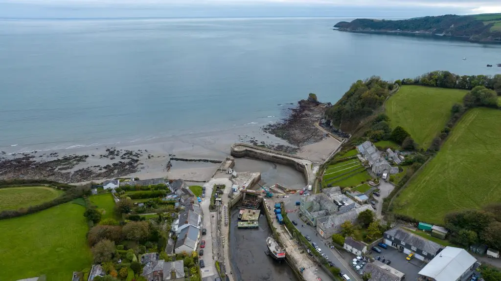 A high drone shot with the harbour in the foreground looking out to sea. St Austell bay is calm and turquoise.