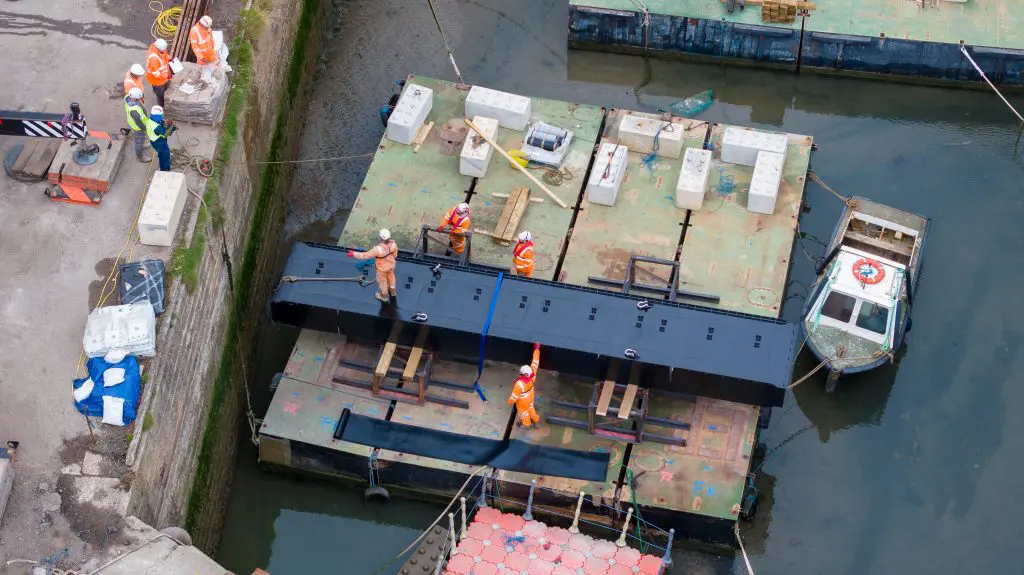 A view from above as the first section of the new lock gate is secured to a floating pontoon by workers in high vis.