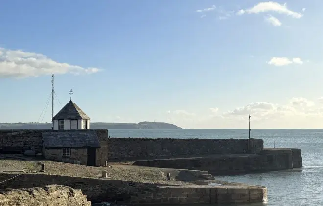 A winter scene looking out across the outer harbour at Charlestown past the historic Roundhouse and on to distant headlands. The tide is high and the sky is crisp and blue.